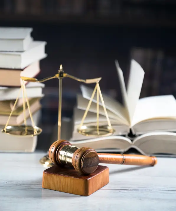 A wooden gavel rests on a square block, with a golden balance scale and partially opened books in the background, symbolizing justice